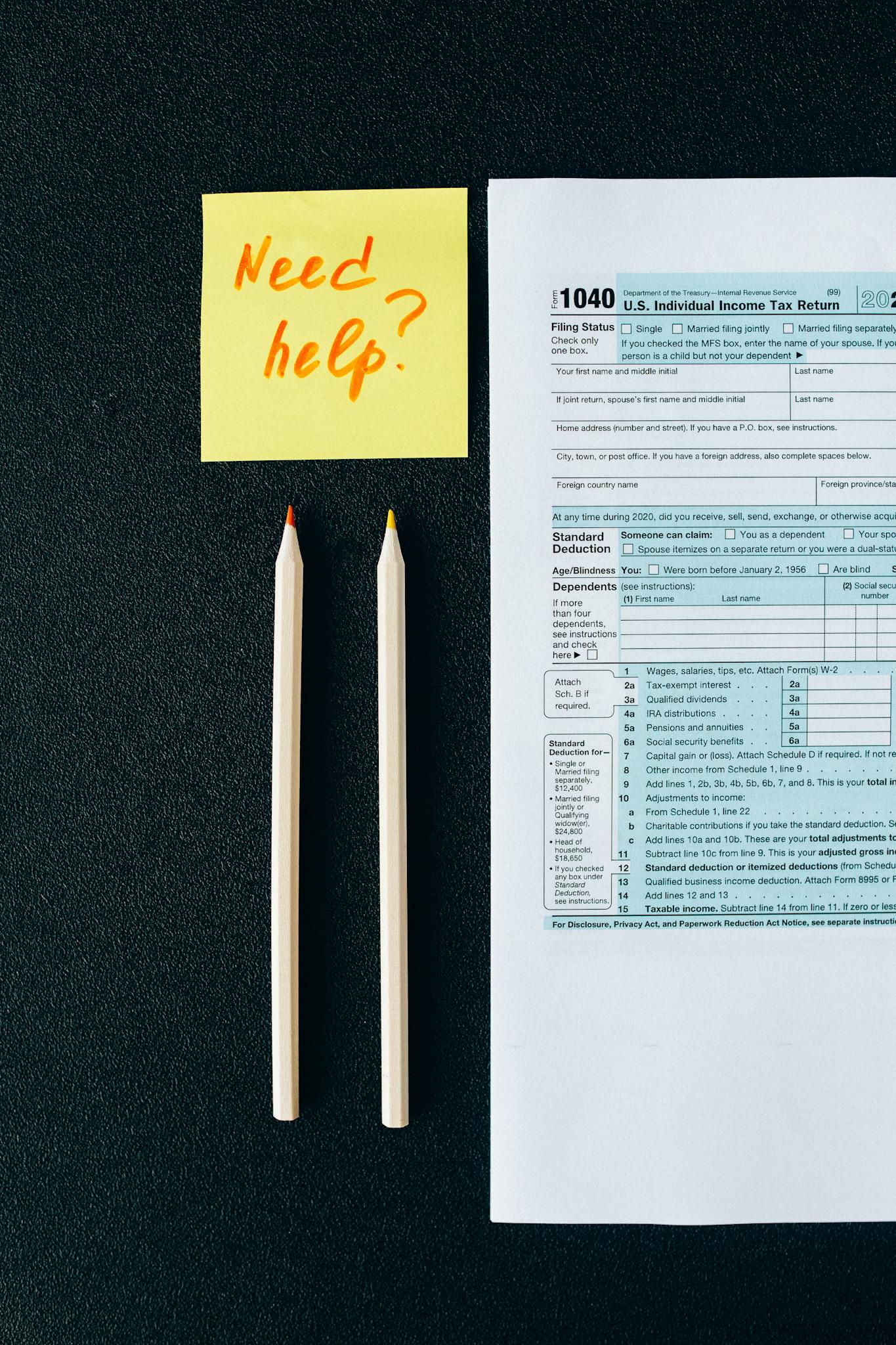 A tax form 1040 with a 'Need help?' sticky note and pencils on a black surface.